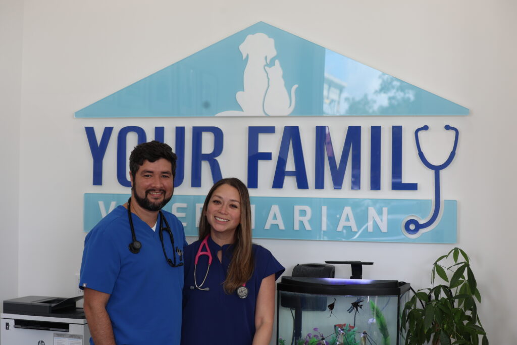 Two Your Family Vet veterinary team members posing before clinic logo with stethoscopes.